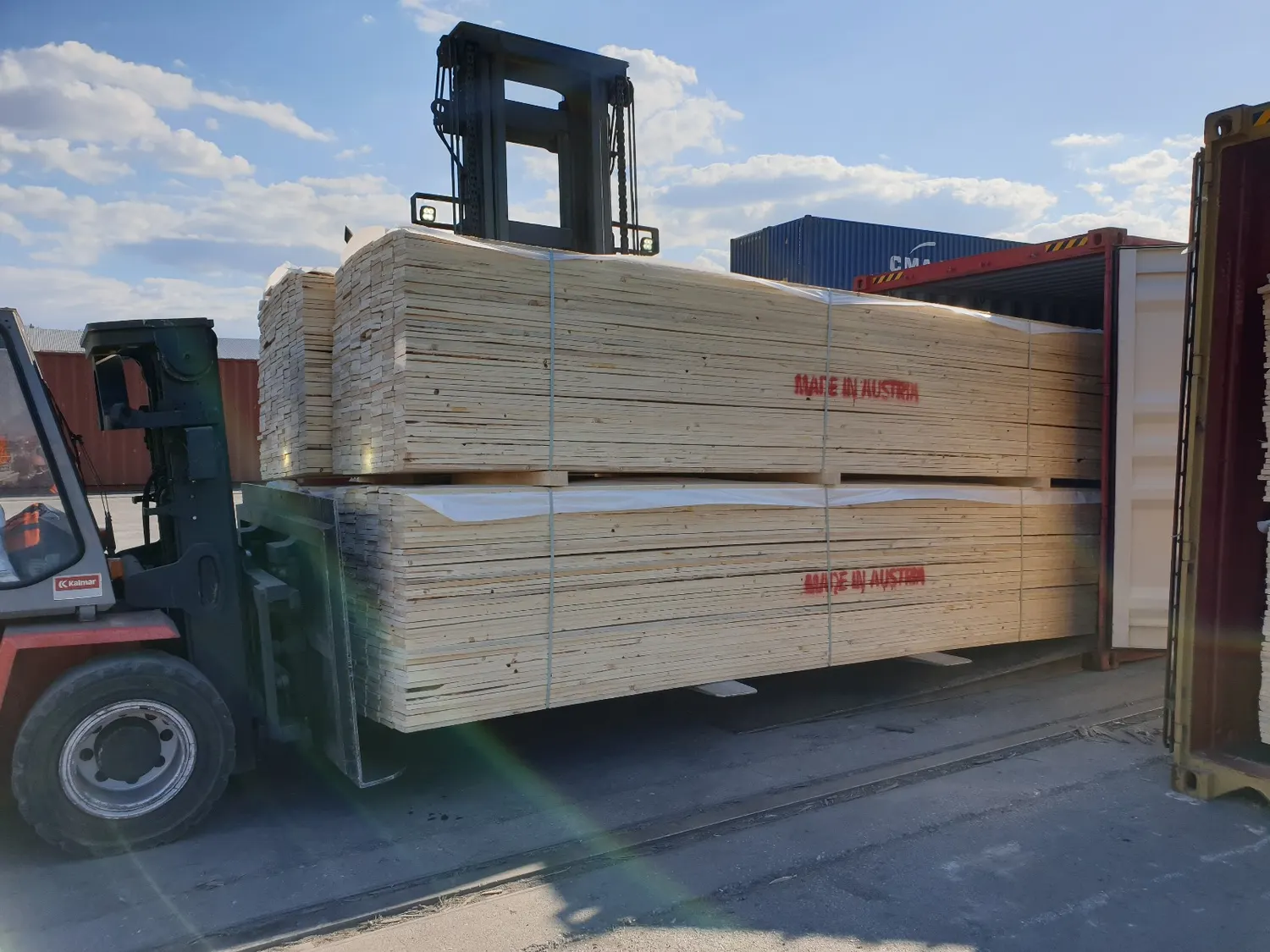 A forklift carrying packs of timber past stacked containers
