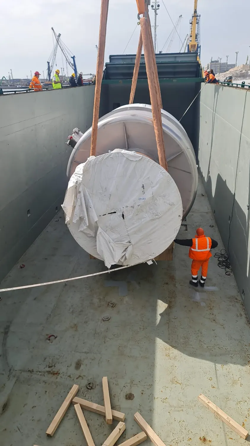 A wrapped reel being lowered into a ship’s hold on slings